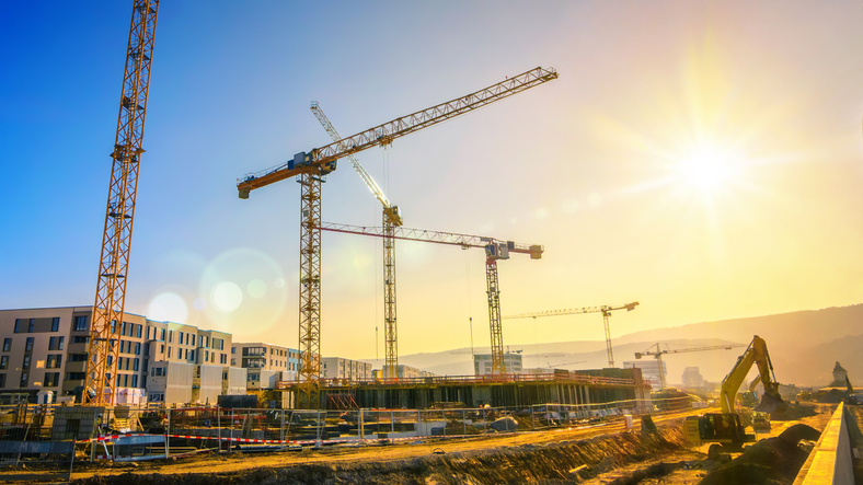 Large construction site including several cranes, with clear sky and the sun Large construction site including several cranes, with clear sky and the sun